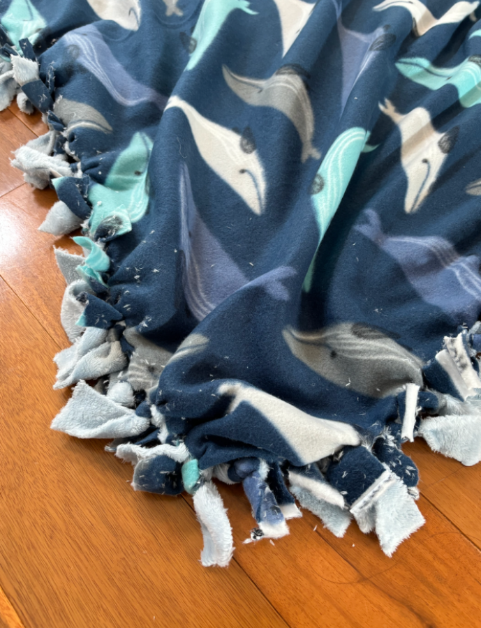 A DIY no-sew blanket in fleece fabric with blue whales on it, in a a close up photo.